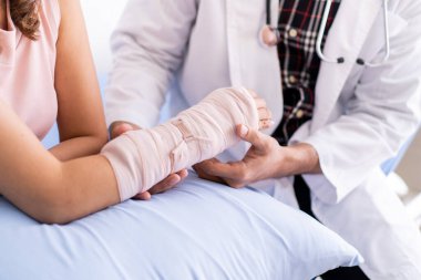 Kemik uzmanı kolundaki bandaj ve bandajla ciddi yaralı kadını muayene ediyor. Doktor, hastanede kırık kollu bir hastayla konuşuyor. Yaralı insan kavramında iyileşme.