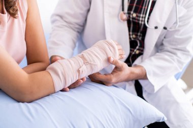 Kemik uzmanı kolundaki bandaj ve bandajla ciddi yaralı kadını muayene ediyor. Doktor, hastanede kırık kollu bir hastayla konuşuyor. Yaralı insan kavramında iyileşme.