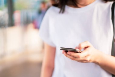 Genç Asyalı kadın kalabalık bir yerde yürürken dokunmatik ekranlı akıllı telefon kullanıyor. Kadın bütün gün sosyal ağa bağımlı. Kadın arkadaşıyla akıllı telefon kullanarak konuşuyordu. Fotoğrafta kopyalama alanı.