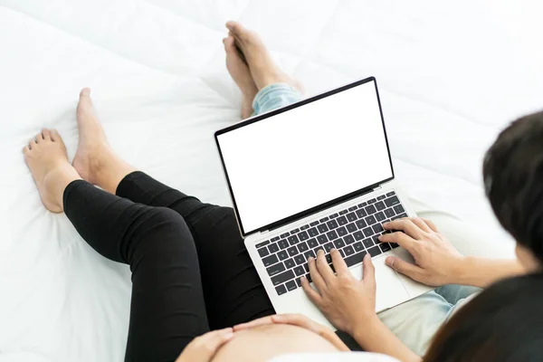 Isolated with clipping path on laptop screen. Romantic husband and wife using laptop computer on the bed to browsing information on the internet. Husband taking care his pregnant wife with affections.