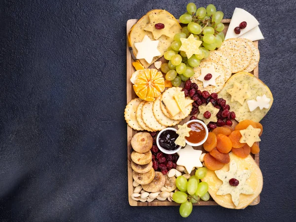 Plato de aperitivos de tabla de queso con varios tipos de plato de queso, uvas, higos secos, arándanos, pistachos y mermeladas sobre fondo oscuro. Vista aérea, espacio libre . —  Fotos de Stock