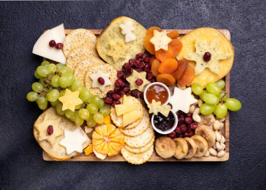 Tahta tabakta çeşitli peynirler sert peynir dilimleri, cevizler, üzümler, krakerler, mango, reçel, koyu arka plan, üst manzara. Boşluğu kopyala.