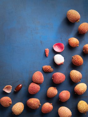 Lychee exotic fruits, organic, fresh and peeled showing the red skin and white flesh on trend classic blue color background, top view, copy space. clipart
