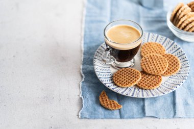 Hollanda karamelli mini stroopwafels, açık gri arka planda şuruplu kurabiyeler ve fotokopi alanı olan bir bardak kahve. Seçici odak.