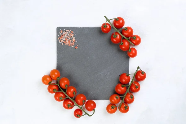 Gray slate board with vine tomatoes, pink salt, light over cement texture background with copy space. Free space for menu or recipes. Cooking or food background. Top view.