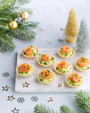 Noel süslemeleri ile birlikte arka planda somon avokado krem peynirli bayram aperatifleri. Yeni yıl ve Noel tatili için şenlikli masa tarifi fikirleri.