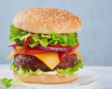 İçinde et, soğan, domates, peynir, hafif arkaplanda taze yeşil salata ve fotokopi alanı bulunan lezzetli bir hamburger sandviçi. Fast food ve barbekü koleksiyonu. Yatay.