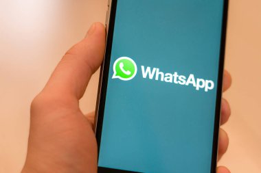 Miami / ABD - 19 Şubat 2020: Ekranda Sosyal medya Whatsapp logosu olan siyah telefon. Haber medyası ikonu. Telefonla el ele. Pazarlama veya iş konsepti için illüstrasyon olarak kullanılabilir