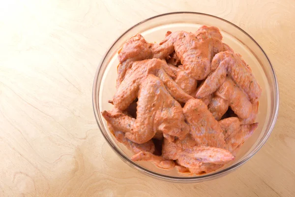 Marinated chicken wings in a glass bowl. Glass dish with marinated wings on a wooden table.