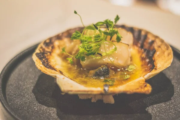 Hokkaido scallop butter yaki in a shell on a black plate — Stock Photo, Image