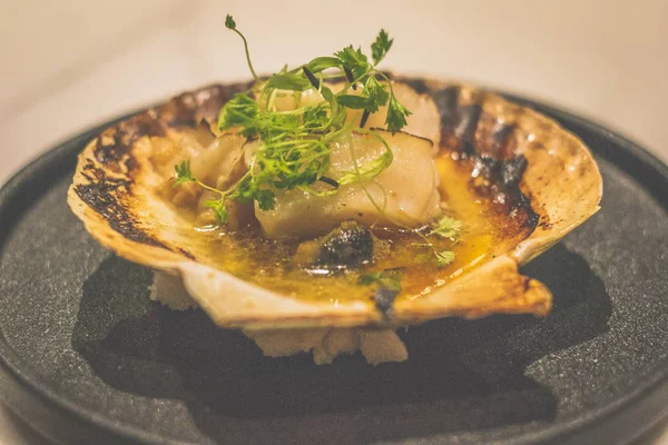 Hokkaido scallop butter yaki in a shell on a black plate — Stock Photo, Image