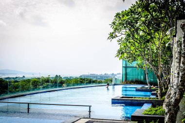 Güneş banyosu sandalyeleri ve ağaçları olan sonsuz yüzme havuzu.