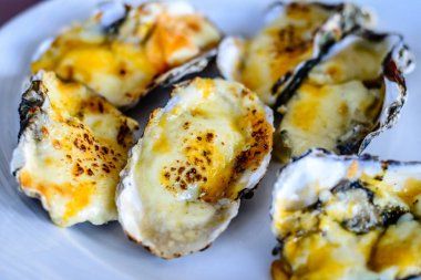 Büyük beyaz bir tabakta peynirli istiridye.