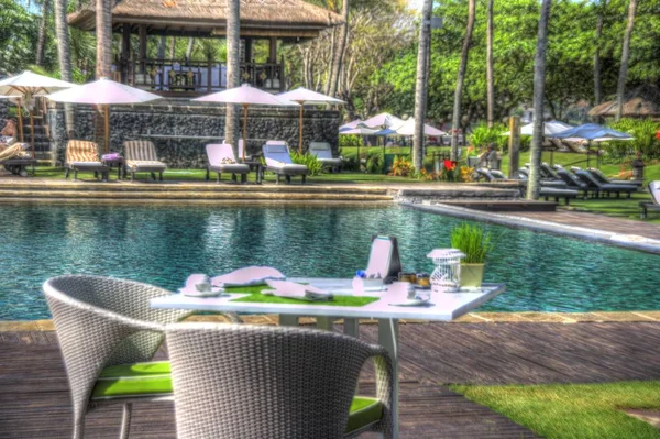 garden table seating with napkins and tableware beside a swimming pool