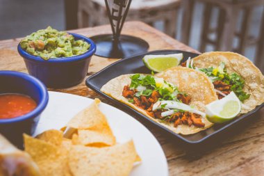 Kızarmış domuz eti, taze soğan ve yanında limon dilimleri, yanında da tortilla cipsi ve guacamole ile Al Pastor Tacos.