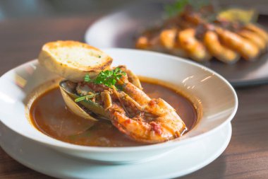 Karidesli deniz ürünleri çorbası. İstiridye ve sarımsaklı ekmek beyaz bir porselen kasede.