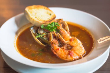 Karidesli deniz ürünleri çorbası. İstiridye ve sarımsaklı ekmek beyaz bir porselen kasede.