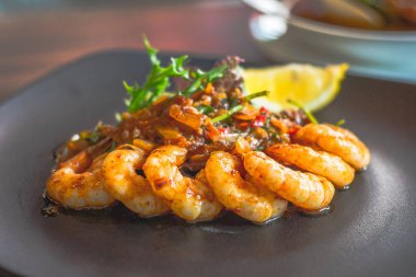 Siyah tabakta limon dilimiyle servis edilen Gambas al jillo sarımsaklı karides.