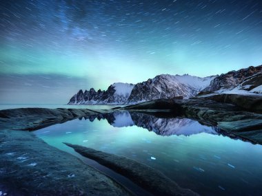 Tungeneset rocks and Aurora Borealis light. Stars trails and northern light. Reflections on the water surface. Senja islands, Norway. Travel - image clipart