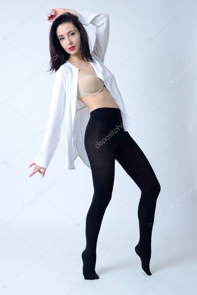 Brave and confident woman from Poland. Young female posing in studio, wearing black tights, white shirt and bra.