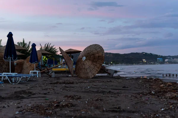 Kasırgadan sonra plaj. Şiddetli yağmurdan sonra plajda pembe gün batımı. Şemsiyeler ıslak kumda yatar..