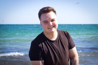 Genç yakışıklı adam güneşli bir yaz gününde deniz kıyısında yürüyor.