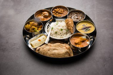 Indian vegetarian Food Thali or platter includes paneer butter masala, dal makhani / tarka, chole papad, kofta curry, gulab jamun, aloo-gobi sabji, chapati and rice with Bengali sweet served clipart