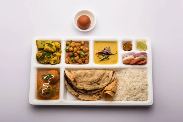 Indian vegetarian Food Thali or Parcel food-tray with compartments in which Malai Kofta, chole, Dal tarka, dry aloo sabji, chapati and rice with sweet gulab jamun served