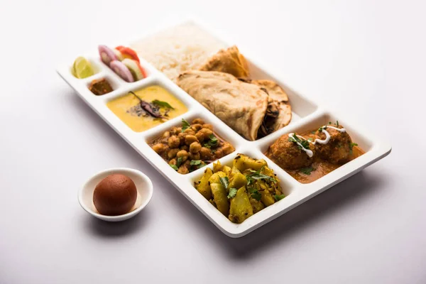 Indian vegetarian Food Thali or Parcel food-tray with compartments in which Malai Kofta, chole, Dal tarka, dry aloo sabji, chapati and rice with sweet gulab jamun served