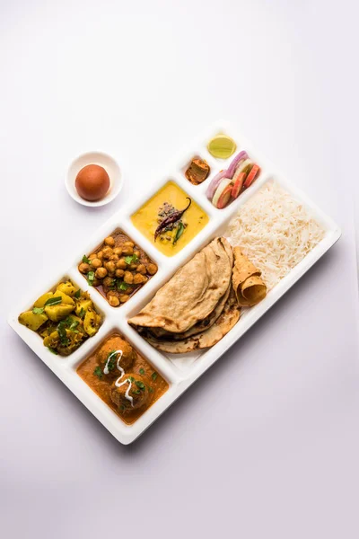 Indian vegetarian Food Thali or Parcel food-tray with compartments in which Malai Kofta, chole, Dal tarka, dry aloo sabji, chapati and rice with sweet gulab jamun served