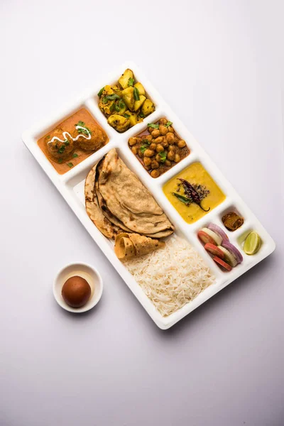 Indian vegetarian Food Thali or Parcel food-tray with compartments in which Malai Kofta, chole, Dal tarka, dry aloo sabji, chapati and rice with sweet gulab jamun served