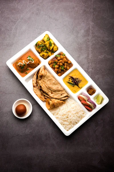 Indian vegetarian Food Thali or Parcel food-tray with compartments in which Malai Kofta, chole, Dal tarka, dry aloo sabji, chapati and rice with sweet gulab jamun served