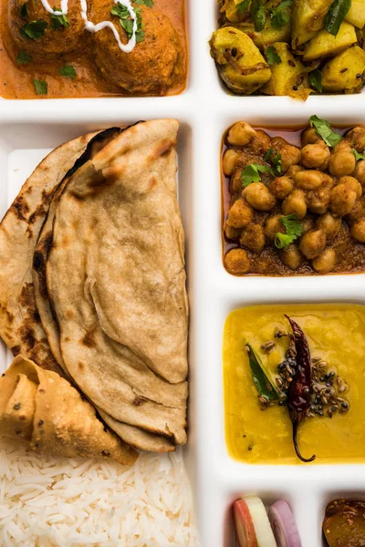 Indian vegetarian Food Thali or Parcel food-tray with compartments in which Malai Kofta, chole, Dal tarka, dry aloo sabji, chapati and rice with sweet gulab jamun served