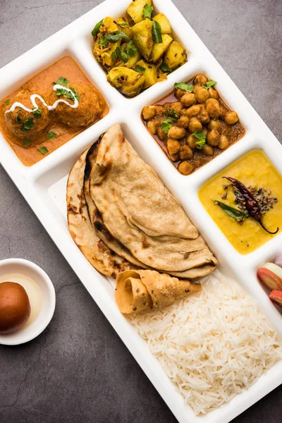 Indian vegetarian Food Thali or Parcel food-tray with compartments in which Malai Kofta, chole, Dal tarka, dry aloo sabji, chapati and rice with sweet gulab jamun served