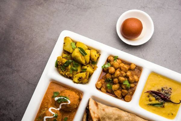 Indian vegetarian Food Thali or Parcel food-tray with compartments in which Malai Kofta, chole, Dal tarka, dry aloo sabji, chapati and rice with sweet gulab jamun served