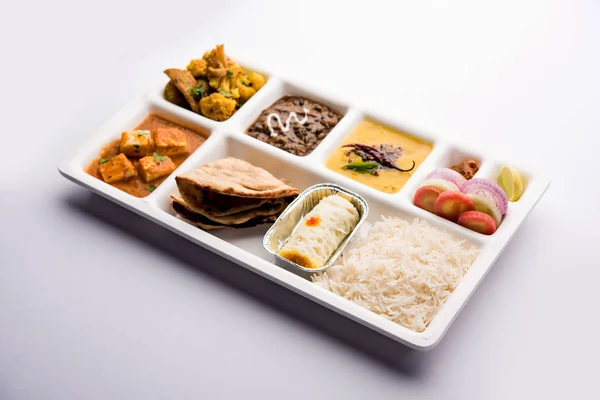 Indian vegetarian Food Thali or Parcel food-tray with compartments in which paneer, dal makhani / parka, aloo-gobi sabji, chapati and rice with Bengali sweet and salad served