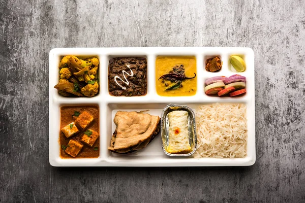 Indian vegetarian Food Thali or Parcel food-tray with compartments in which paneer, dal makhani / parka, aloo-gobi sabji, chapati and rice with Bengali sweet and salad served