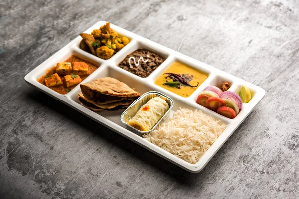 Indian vegetarian Food Thali or Parcel food-tray with compartments in which paneer, dal makhani / parka, aloo-gobi sabji, chapati and rice with Bengali sweet and salad served