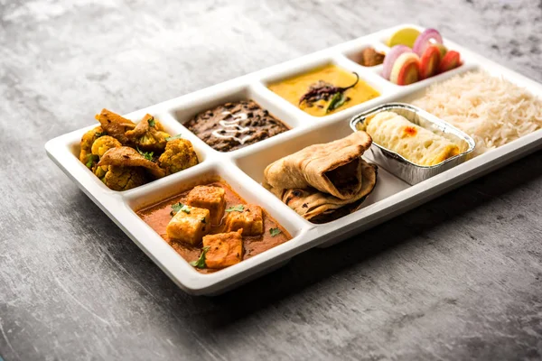 Indian vegetarian Food Thali or Parcel food-tray with compartments in which paneer, dal makhani / parka, aloo-gobi sabji, chapati and rice with Bengali sweet and salad served