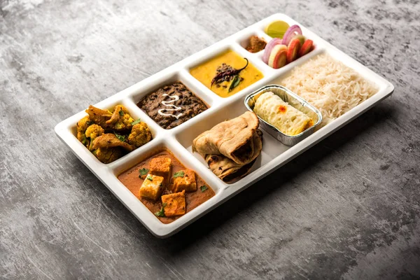 Indian vegetarian Food Thali or Parcel food-tray with compartments in which paneer, dal makhani / parka, aloo-gobi sabji, chapati and rice with Bengali sweet and salad served