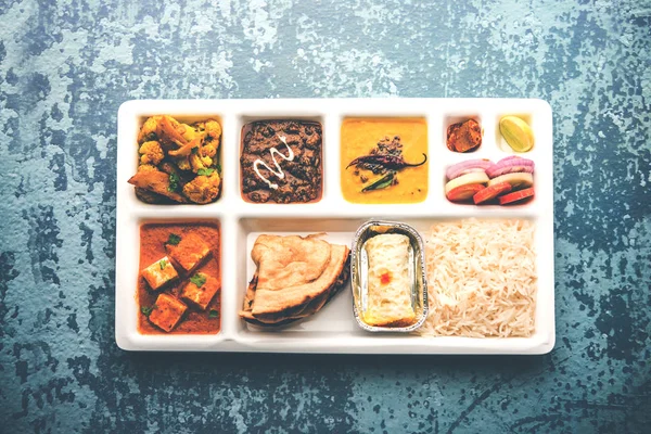 Indian vegetarian Food Thali or Parcel food-tray with compartments in which paneer, dal makhani / parka, aloo-gobi sabji, chapati and rice with Bengali sweet and salad served