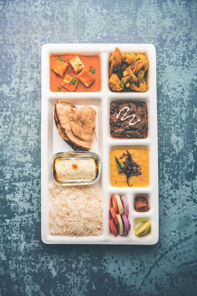 Indian vegetarian Food Thali or Parcel food-tray with compartments in which paneer, dal makhani / parka, aloo-gobi sabji, chapati and rice with Bengali sweet and salad served