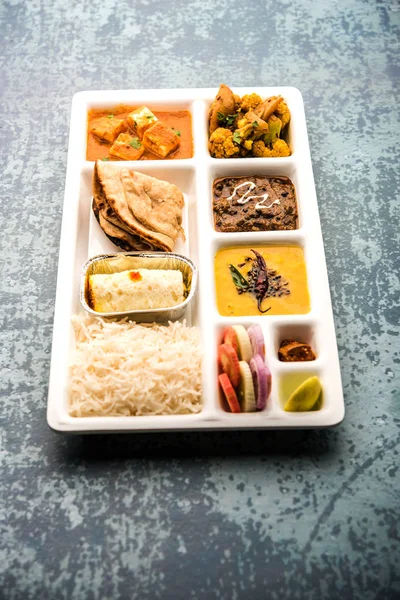 Indian vegetarian Food Thali or Parcel food-tray with compartments in which paneer, dal makhani / parka, aloo-gobi sabji, chapati and rice with Bengali sweet and salad served