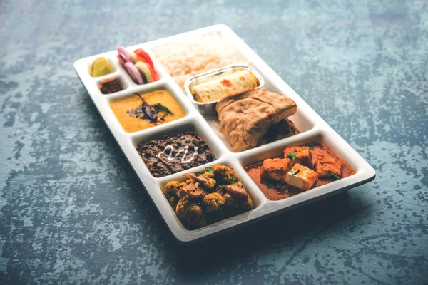 Indian vegetarian Food Thali or Parcel food-tray with compartments in which paneer, dal makhani / parka, aloo-gobi sabji, chapati and rice with Bengali sweet and salad served