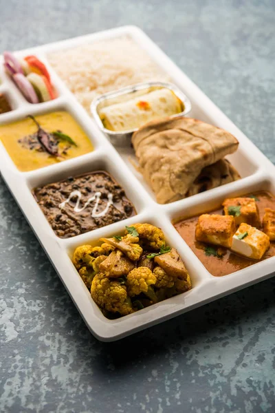 Indian vegetarian Food Thali or Parcel food-tray with compartments in which paneer, dal makhani / parka, aloo-gobi sabji, chapati and rice with Bengali sweet and salad served