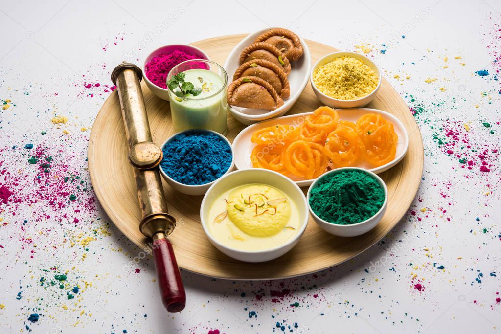 Happy Holy concept  showing Indian assorted sweets like jalebi, gujiya, than, ras malai with holi colours and pichkari, isolated over white background