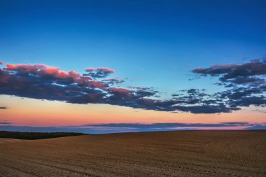 Akşam kırsal manzarası - mavi gökyüzü ve gün batımında saban tarlaları üzerinde bulutlar.