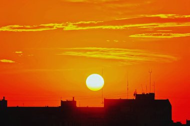 Manzara - güneş batımında bulutlu, çatıları siluetleri ön plan.