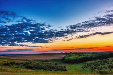 Akşam kırsal manzara - mavi gökyüzü günbatımı meadows, orman ve sürülmüş alanlar üzerinde bulutlara ile.