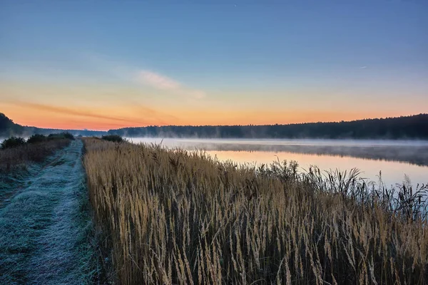 Autumn landscape - morning twilight over the lake. Fog over the water, the grass covered with frost.